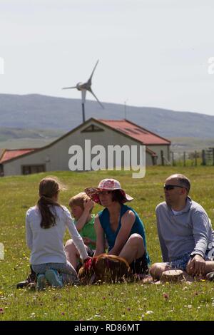 Famiglia rilassante godendo la visione di sport competitivo come parte del Festival Berneray taing posto sulla fioritura machir , precedentemente in estate habitat di nidificazione di poco sterne . Sala comunitaria del Borve dietro con fonti di energia rinnovabili turbina eolica . Foto Stock