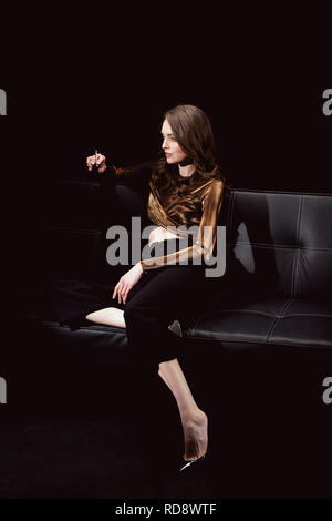 Bella donna glamour seduta sul lettino e il fumo di sigaretta su isolato nero Foto Stock