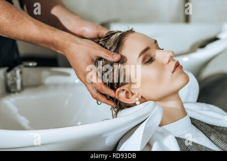 Vista parziale di un parrucchiere lavaggio di capelli attraente giovane donna nel salone di bellezza Foto Stock