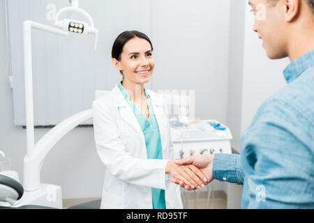 Donna sorridente dentista stringono le mani con African American paziente Foto Stock