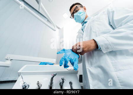 African American dentista in bicchieri e maschera indossando guanti di lattice Foto Stock