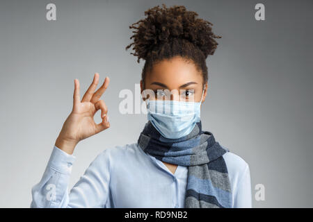 La donna che mostra bene gesto. Foto di sano americano africano donna indossa la maschera protettiva contro le malattie infettive e l'influenza. Health care concetto. Foto Stock