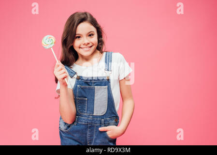 Allegro kid holding lollipop con la mano in tasca isolato in rosa Foto Stock