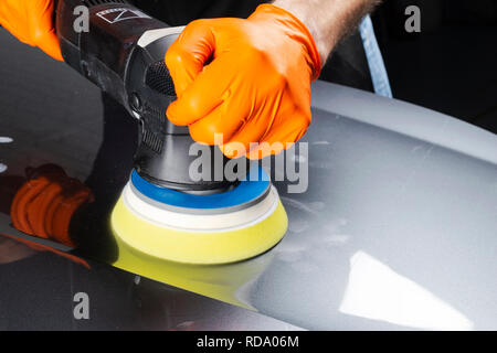 Auto cera polacco lavoratore mani applicando il nastro protettivo prima della lucidatura. Pulitura e lucidatura auto. Dettagli auto. Chi detiene un lucidante in mano e Foto Stock