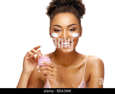 Bella donna usando la crema idratante. Foto di sorridere americano africano donna su sfondo bianco. La cura della pelle e concetto di bellezza Foto Stock