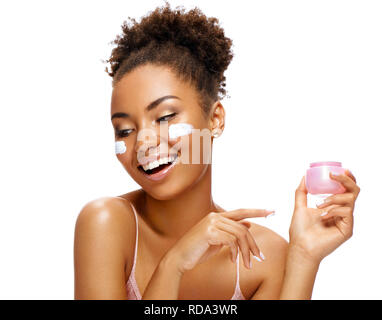 Donna sorridente con crema idratante sulla sua faccia. Foto di African American donna con pelle sana isolati su sfondo bianco. Bellezza e cura della pelle Foto Stock