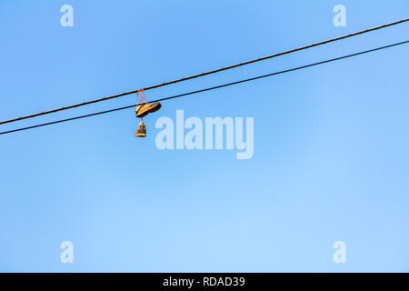 Vecchio sneakers appeso su un filo elettrico di cielo blu in background in una giornata di sole Foto Stock