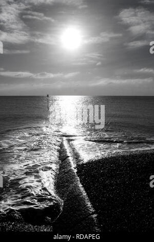 Fotografia in bianco e nero della bassa inverno sole che splende su una superficie piana di mare calmo, un lungo e alto luce che riflette sul mare e su una lunga pausa mare hal Foto Stock