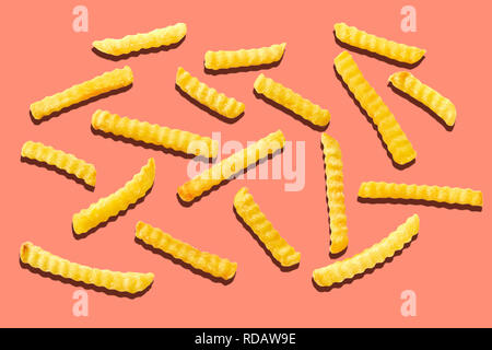 Croccante crinkle cut potato chips, pommes frites o patatine fritte sparse in maniera casuale su uno sfondo arancione nella parte piana di laici vista aerea Foto Stock