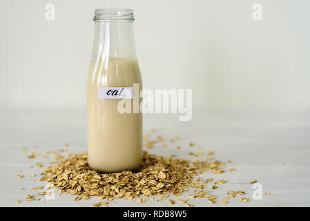 Bottiglia di vetro di latte di avena su sfondo bianco dietro mucchio di fiocchi di avena Foto Stock