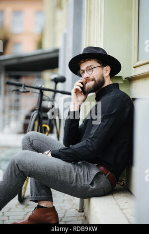 Bello barbuto imprenditore in abito classico è utilizzando uno smart phone e sorridenti mentre cavalcate in bicicletta in città Foto Stock