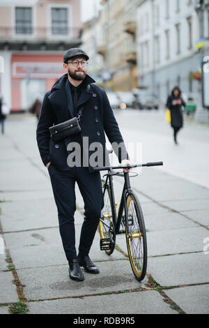 Un giovane sorridente imprenditore elegante spingendo una bicicletta mentre va al lavoro. Foto Stock