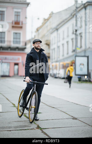 Un giovane sorridente imprenditore elegante spingendo una bicicletta mentre va al lavoro. Foto Stock