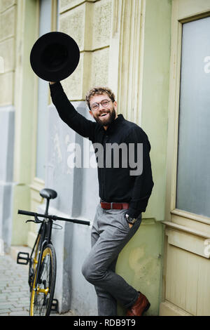 Felice giovani hipster uomo con fixed gear bike agitando la mano sulla strada di città Foto Stock
