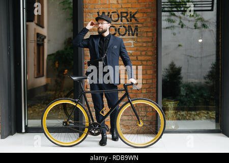 Lo stile di vita, il trasporto di persone e di concetto. giovane uomo in occhiali da sole equitazione Bicicletta su una strada di città oltre brickwall Foto Stock