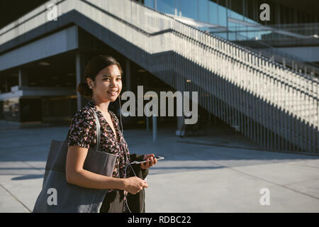 Sorridente Asian studente universitario camminando sul campus ascolto di musica Foto Stock