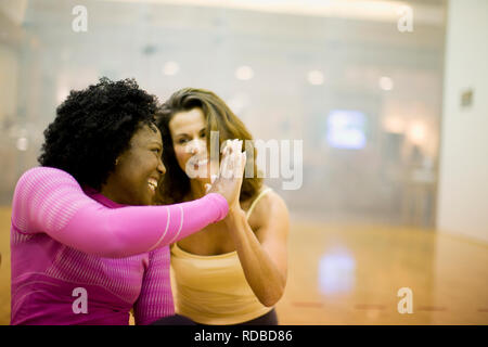 Due donna sorridente dando a ogni altro ad alta cinque all'interno di uno studio di yoga. Foto Stock