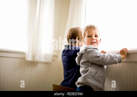 Due fratelli guardando fuori dalla finestra della loro casa. Foto Stock