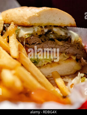 Steak sandwich tagliato a metà con il formaggio, lattuga, pomodoro, peperoni e cipolle. Patatine fritte e panino in rosso cesto in plastica con rivestimento di carta Foto Stock