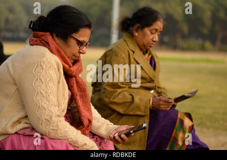 Nord e sud indiane senior donne anziane utilizzando la tecnologia occupato sul loro smartphone in un parco all'aperto a Delhi inverni. Foto Stock