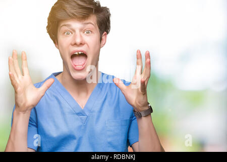 Giovane medico medico che indossano uniformi su sfondo isolato celebrando crazy e sorpreso per il successo con le braccia sollevate e aprire gli occhi urlando excite Foto Stock