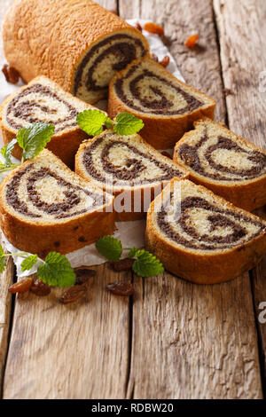 Tagliate a fette il papavero rotolo con uvetta e decorate con la menta close-up su pergamena su una tavola di legno verticale. Foto Stock