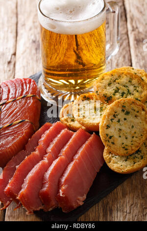 Birra Leggera o Birra Light con schiuma, tonno affumicato e pane tostato con aglio e verdi closeup sul piano verticale. Foto Stock