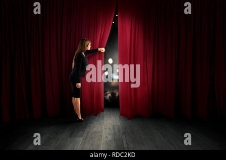 Donna aprire tende rosse del palcoscenico teatrale Foto Stock