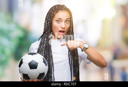 Giovani capelli intrecciati African American Girl tenendo palla calcio su sfondo isolato con sorpresa faccia puntare il dito a se stesso Foto Stock