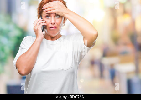 Accattivante senior redhead caucasica donna parlando sullo smartphone su sfondo isolato ha sottolineato con la mano sulla testa, sconvolto con vergogna e la sorpresa f Foto Stock