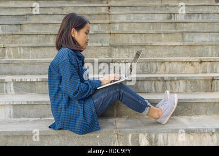 Studente seduto sui gradini di scale, mettendo laptop sulla coscia Foto Stock