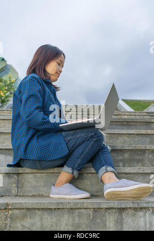 Studente ragazza utilizzando laptop, sedersi sulle scale nel campus Foto Stock