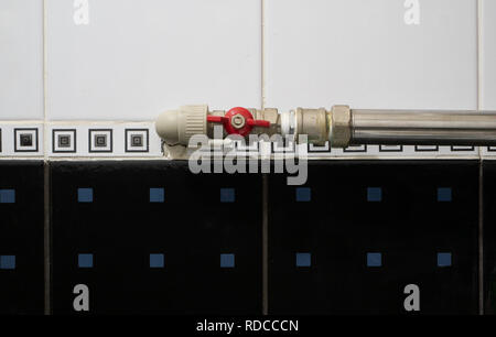 Piccolo rosso conduttura di acqua valvola sul tubo in bagno con nero e bianco delle piastrelle di ceramica sulla parete Foto Stock
