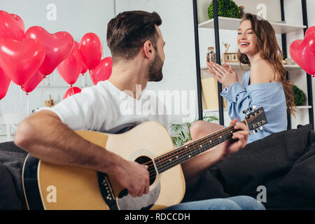 Coppia felice per celebrare San Valentino mentre il giovane uomo suonare la chitarra acustica Foto Stock