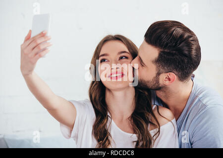 Fidanzato bacio ragazza tenendo selfie in camera da letto Foto Stock