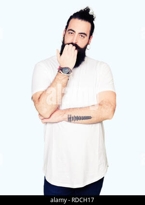 Tanga giovane uomo con i capelli lunghi e la barba che indossa casual t-shirt bianco cercando stressato e nervoso con le mani sulla bocca di mordere le unghie. Problema di ansia Foto Stock