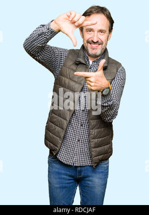 La mezza età uomo bello indossare Gilet invernale sorridente rendendo il telaio con le mani e le dita con la faccia felice. La creatività e il concetto di fotografia. Foto Stock