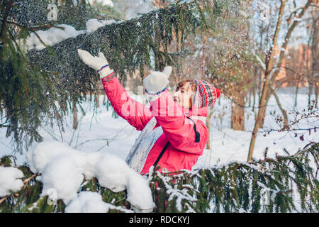 Senior donna gettando la neve in aria a soleggiata giornata invernale nella foresta. Donna con divertimento all'aperto Foto Stock