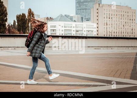 Il capretto con uno zaino pieno di gioia saltando a casa dopo scuola Foto Stock