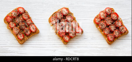 Fette biscottate con burro di arachidi, fragole e chia semi in bianco sullo sfondo di legno. Una sana dieta. Close-up. Foto Stock