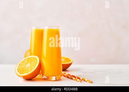 Bevanda estiva. Il succo d'arancia fresco nel bicchiere con fettine di arancia e cannucce su marmo bianco tabella su sfondo rosa. Copia spazio per il testo. Selectiv Foto Stock