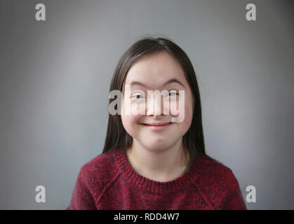 Carino sorridente la sindrome di down girl su sfondo grigio Foto Stock