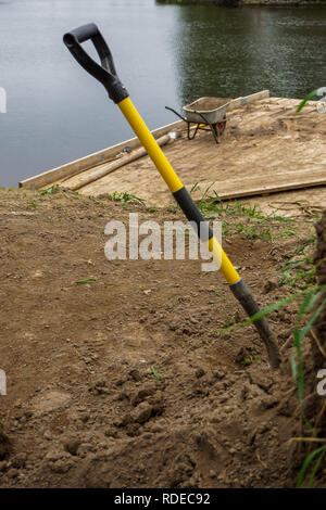 Carriola e la pala per la costruzione nel sito area di costruzione presso il fiume. Costruzione carriola e pala nella sabbia dal fiume Daugava, Latv Foto Stock