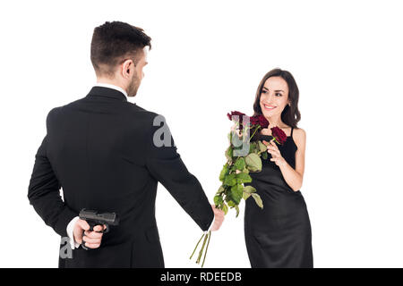 L'uomo regalare fiori rossi alla ragazza nascondendo la pistola dietro la schiena, isolato su bianco Foto Stock