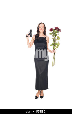 Felice elegante agente segreto in abito nero tenendo la pistola e rose rosse, isolato su bianco Foto Stock