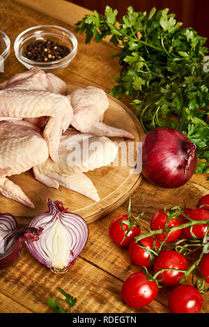 Fresche biologiche di ali di pollo su un tagliere con le spezie e le verdure sul vecchio tavolo in legno. Foto Stock