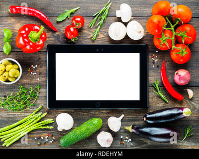 Nero tablet pc e gli ingredienti per cucinare le verdure e le erbe sul tavolo di legno dello sfondo. Vista dall'alto. Copia dello spazio. Concetto di cucina a vista. Digital ricettario. Online il negozio di drogheria concetto. Mockup Foto Stock