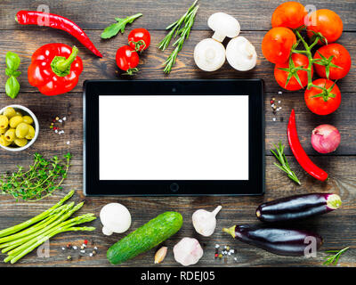 Nero tablet pc e gli ingredienti per cucinare le verdure e le erbe sul tavolo di legno dello sfondo. Vista dall'alto. Copia dello spazio. Concetto di cucina a vista. Digital ricettario. Online il negozio di drogheria concetto. Mockup Foto Stock