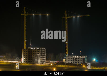 Gru a torre e incompiuta a più piani alti edifici in costruzione di notte illuminata sul sito di costruzione Foto Stock