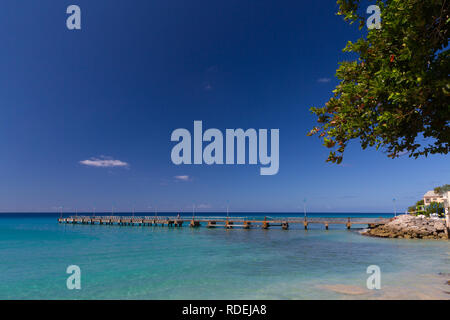 Il molo a Mullins Beach, Barbados si allunga in un mare turchese sotto un cielo blu chiaro. Foto Stock